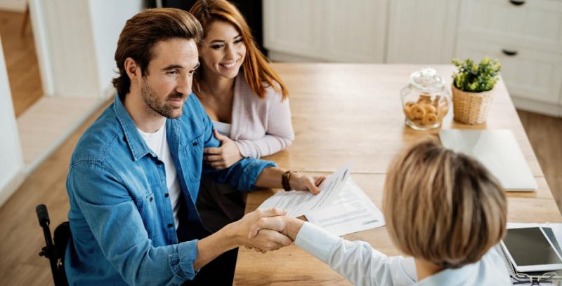 young-happy-couple-making-an-agreement-with-their-insurance-agent-on-a-meeting-at-home-focus-is-on-man-in-wheelchair(1)